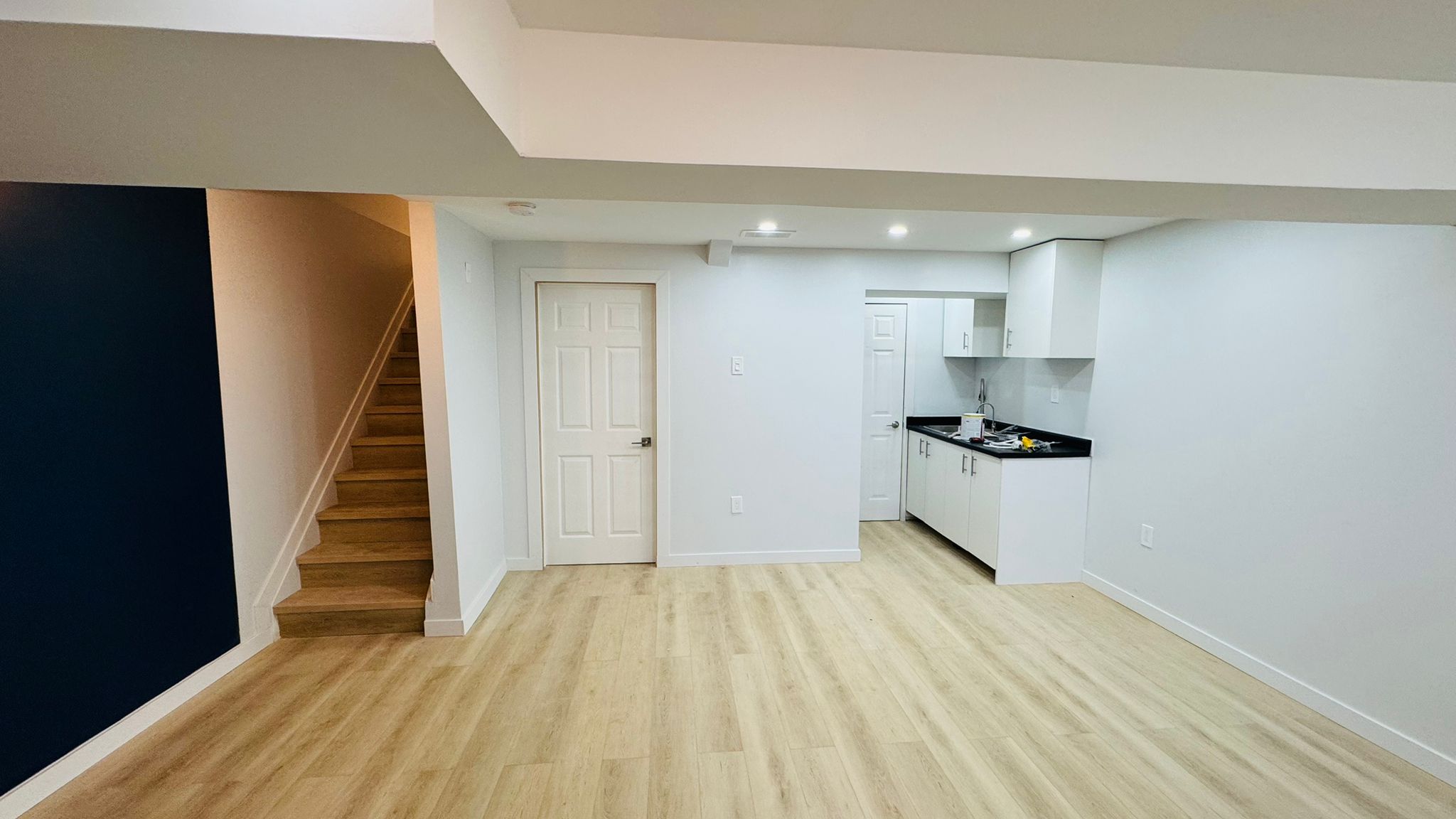 Finished basement with oak-tone vinyl plank flooring, navy accent wall and pot lights