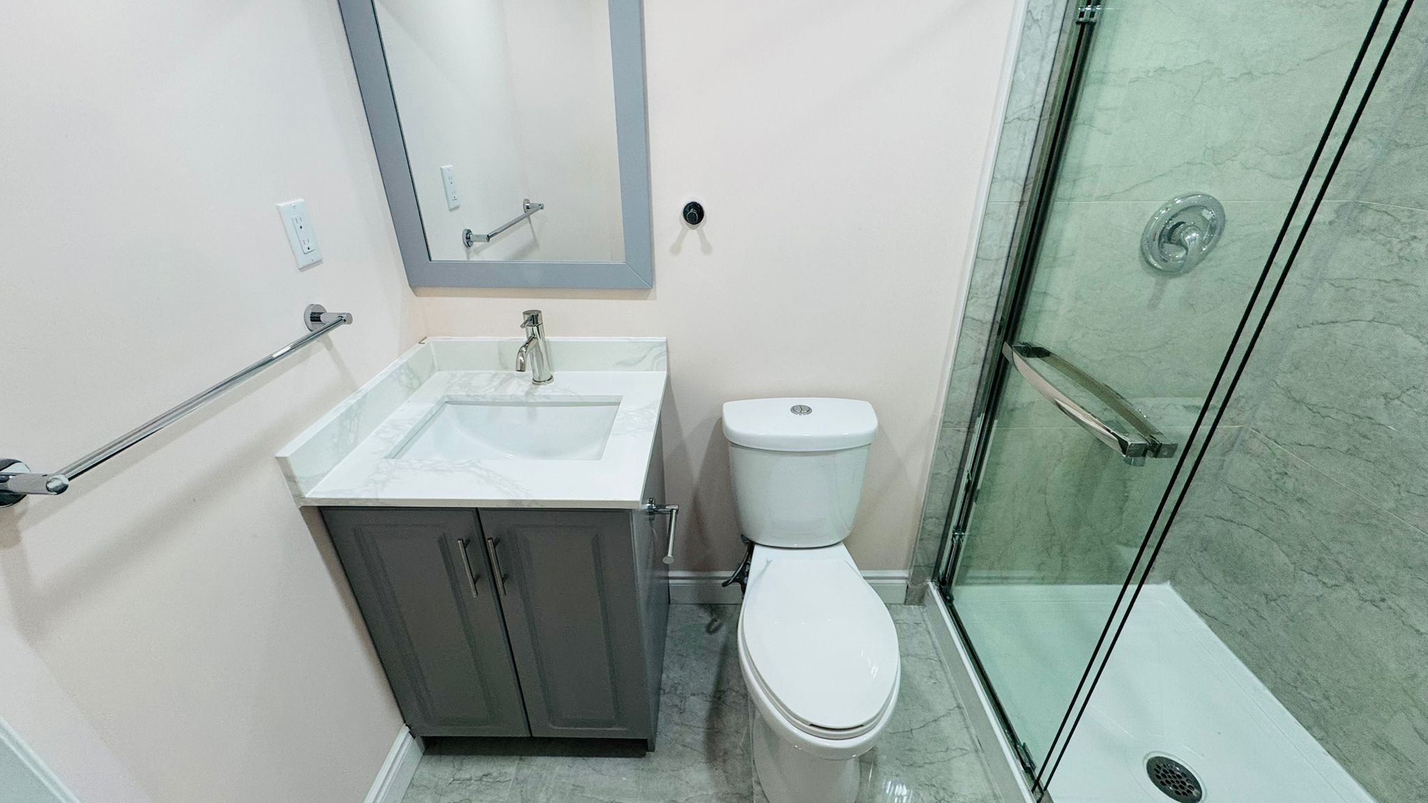 Finished bathroom with a grey shaker vanity, glass shower and marble-look tile