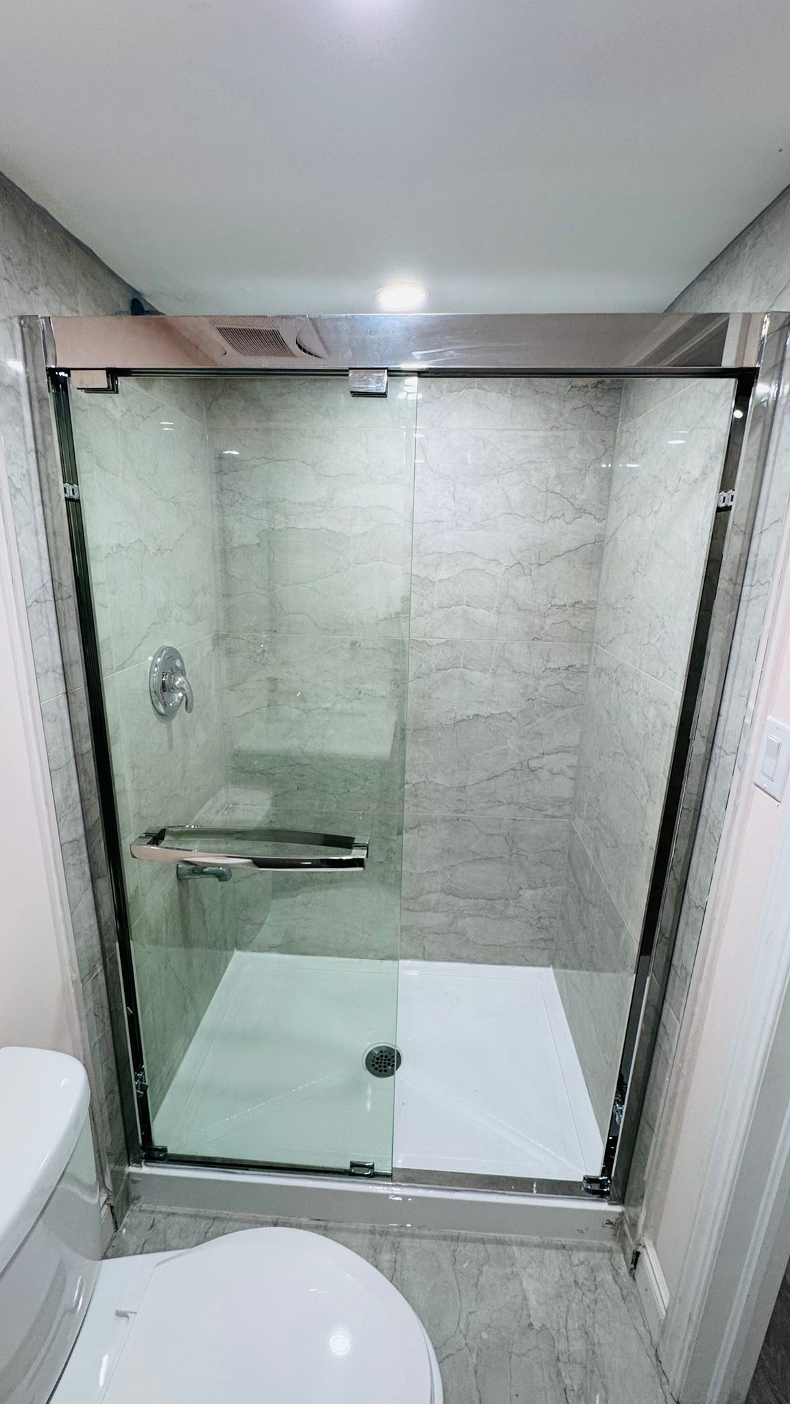 Frameless glass shower enclosure with chrome fixtures and grey tile