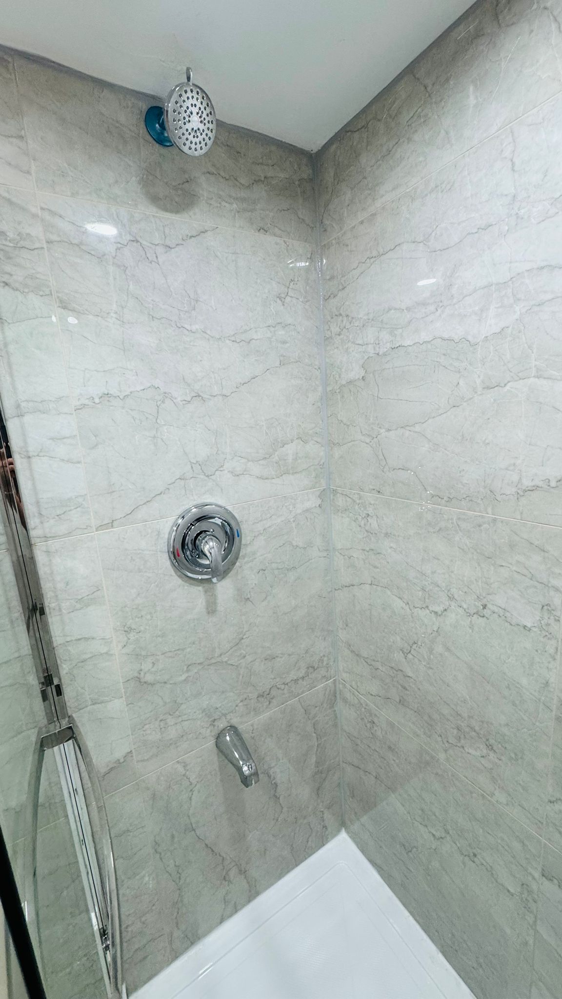 Tiled shower wall with large-format marble-look porcelain and chrome rain head